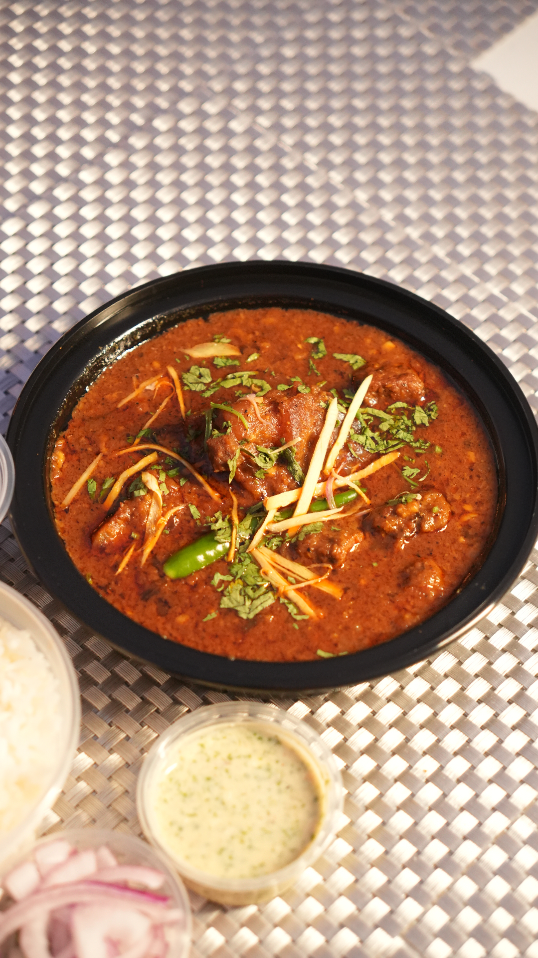 Slow-cooked Punjabi goat curry in a black bowl with ginger garnish