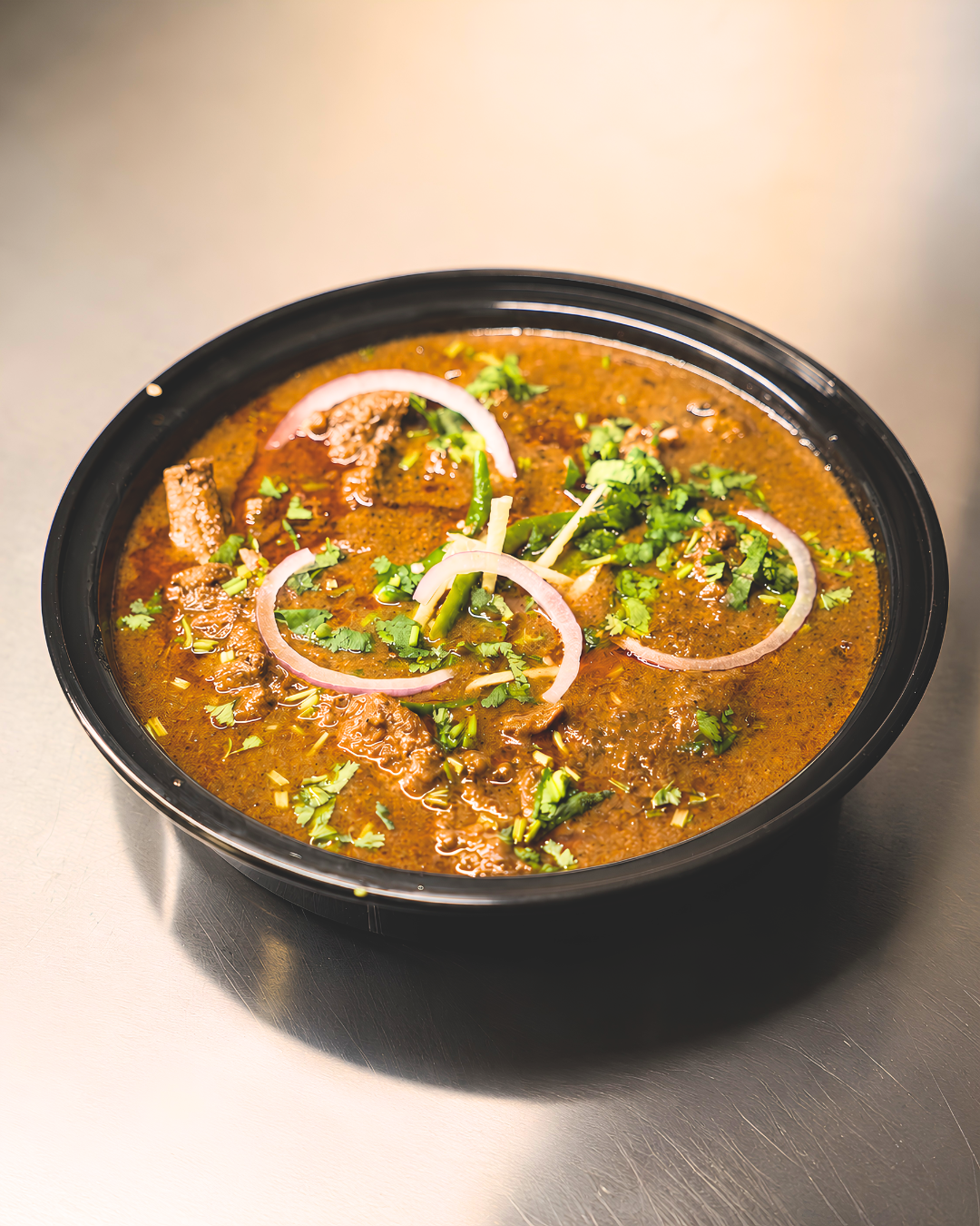 Goat curry topped with onion rings, green chili, and cilantro